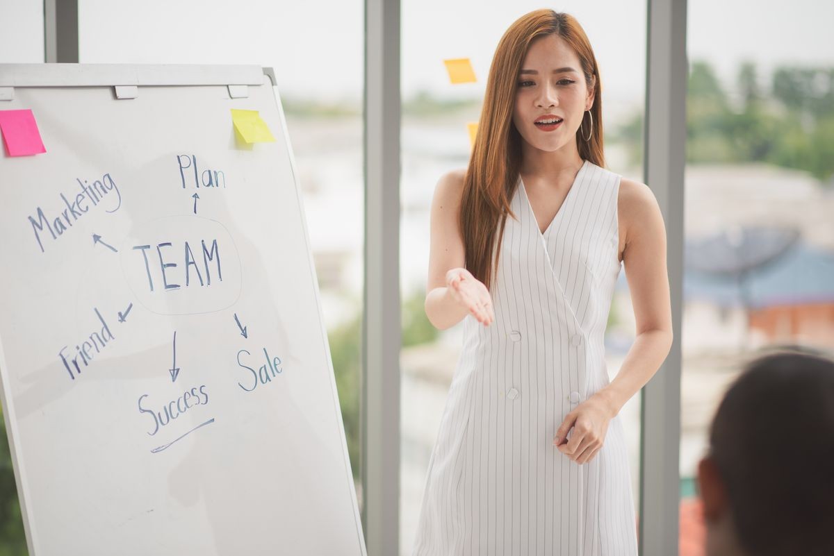 Successful business young woman presenting to employees, business coach giving presentation to clients in meeting room, team leader reporting about work explaining result on whiteboard