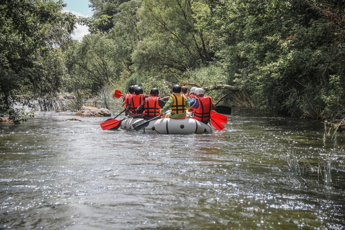 A group of tourists with a guide rafting along the river through the forest on a raft. Rafting on the  Pivdennyi Buh River